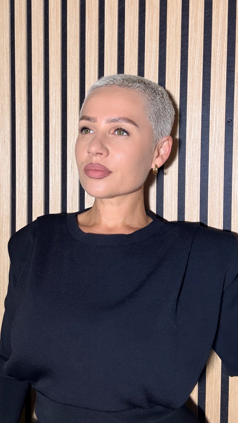 Kiva with platinum hair against a striped wooden wall